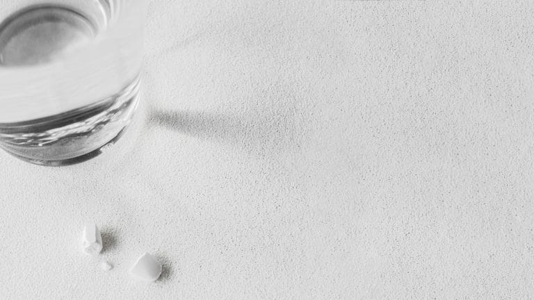 Glass of clear water on a light surface with soft reflections.